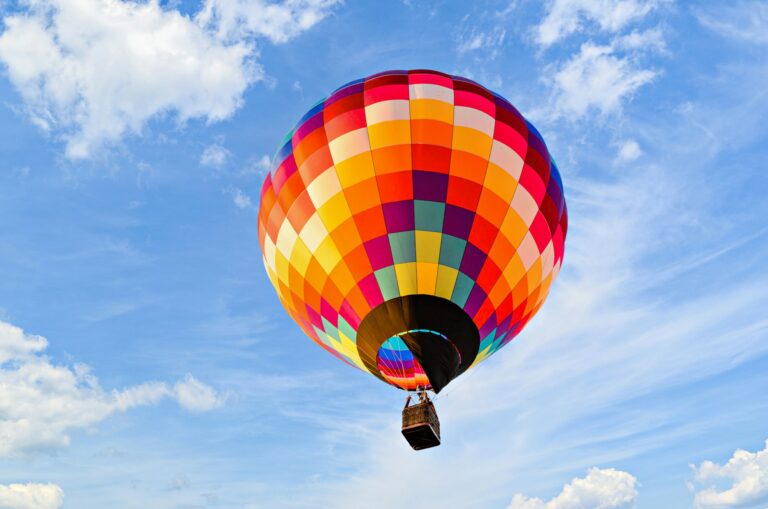 Brightly colored hot air balloon soaring through a bright blue sky, with clouds in the background